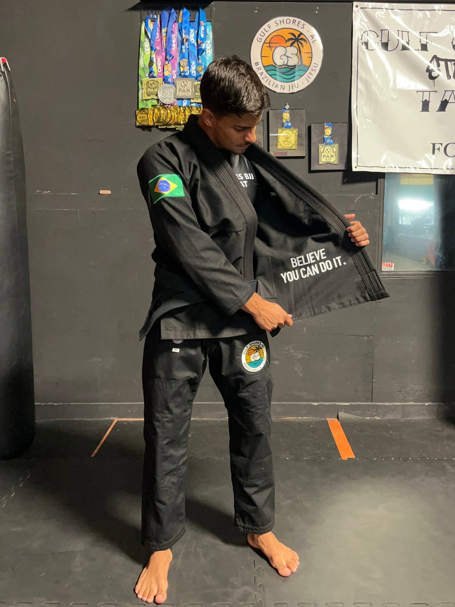 Gulf Shores BJJ coach in a black gi beside the academy medal wall